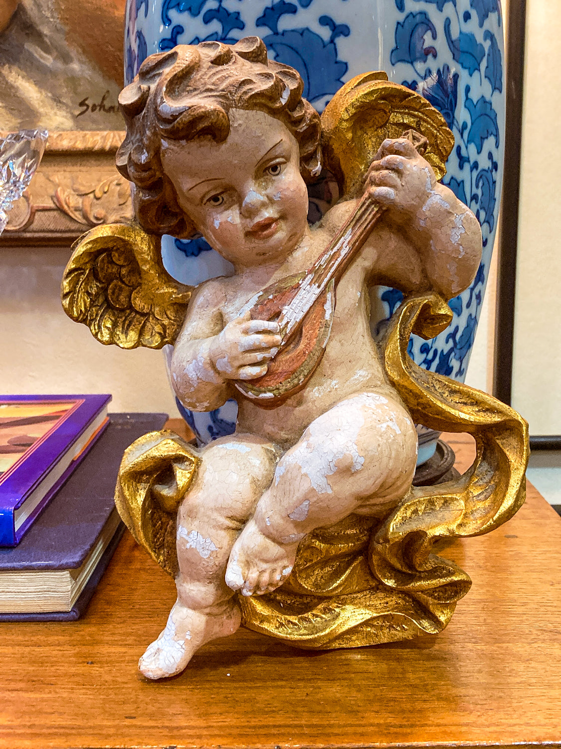 Statue of an angel playing a lyre on a wooden surface with a decorative background. 20th Century Hand Painted Gessoed Gilded Cherub Wall Hanging Sculpture