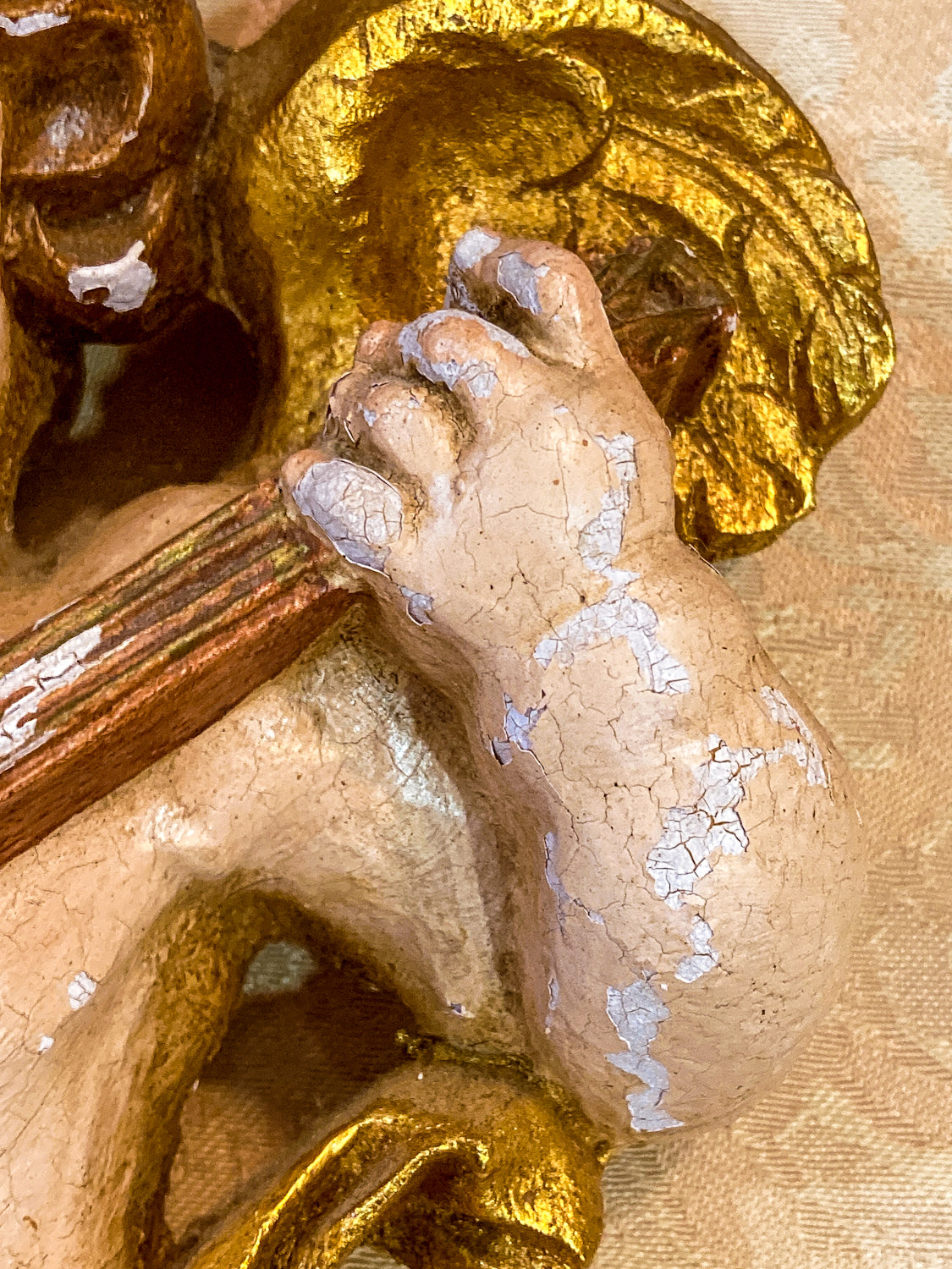 Close-up of a hand holding a musical object with a detailed background 20th Century Hand Painted Gessoed Gilded Cherub Wall Hanging Sculpture