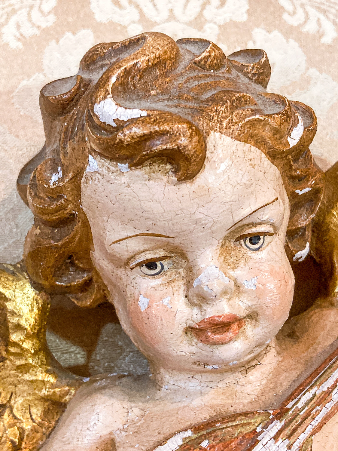 Close-up of a cherub figurine with detailed hair and facial features. 20th Century Hand Painted Gessoed Gilded Cherub Wall Hanging Sculpture